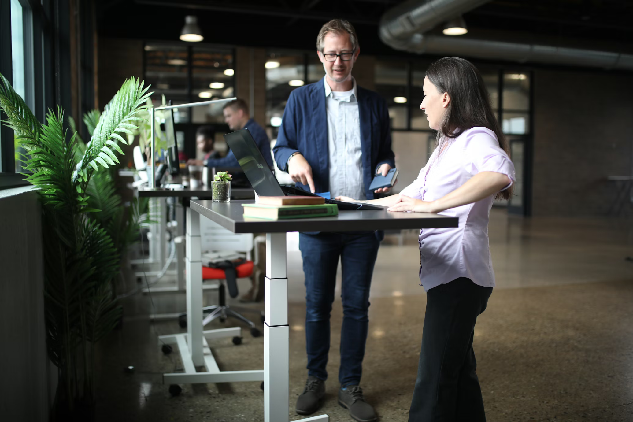 Deux collègues échangent autour d'un bureau assis-debout dans un open space